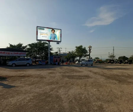 Large billboard promoting ethnic men’s fashion in an open highway area, surrounded by cars, autos, and local shops under clear blue sky.